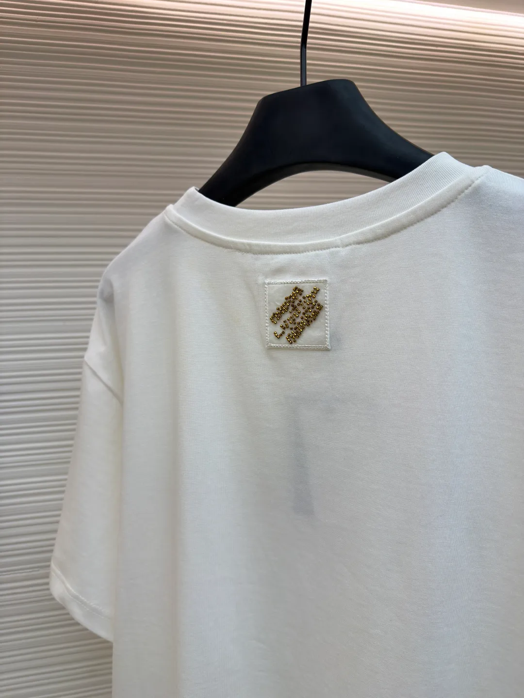 LOUIS VUITTON cotton round neck embroidered Vuitton signature logo short sleeves ●Original version: purchased and developed for 12300 ●Item number: 1682272-A10 ●Fabric: cotton fabric ●Technology: embroidery production ●Color: white ●Version: fitted version ●Weight: about 270 grams ●Size: S-M-L-XL ●Description: This white short-sleeved T-shirt is made of high-count combed cotton fabric and has been treated with pre-washing technology. It has a soft and skin-friendly touch and is not easy to deform. The silhouette of the shirt is a loose shoulder design, which meets the needs of modern casual wear. The core decoration area on the chest uses hand-beading and bronzing technology, and uses metallic gold sequins and embroidery threads intertwined to outline a three-dimensional letter pattern. The sequins are layered and inlaid, and each one is manually positioned and fixed by craftsmen to ensure a regular texture and uniform gloss. The edges of the letters are sewn with matte silk thread to form a visual contrast between gold and matte, while reinforcing the decorative structure to avoid falling off during wear. The neckline uses double-needle hemming technology and is matched with ribbed cuffs of the same fabric. It is durable and fits the neck. The overall craftsmanship combines handicraftsmanship with modern clothing technology, and the details show exquisite texture. The overall wiring is straight and delicate, the fabric is comfortable and soft, and the color is consistent without color difference. It can be matched with the same style to create a fashionable look and control various occasions. Customized accessories, complete with three standards, same style for men and women!
